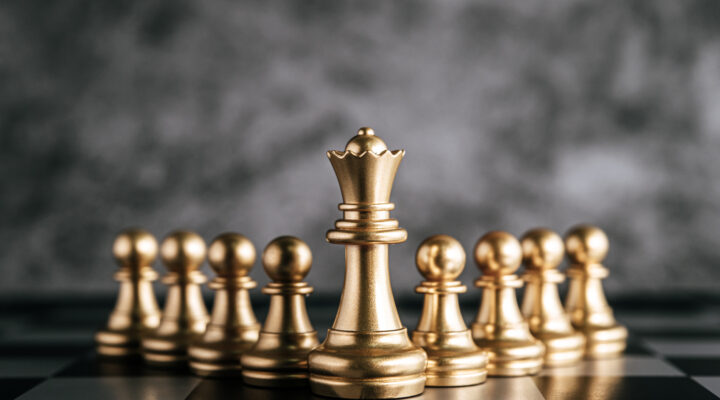 Golden chess pieces on a chess board with a dark grey background.