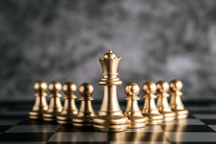 Golden chess pieces on a chess board with a dark grey background.